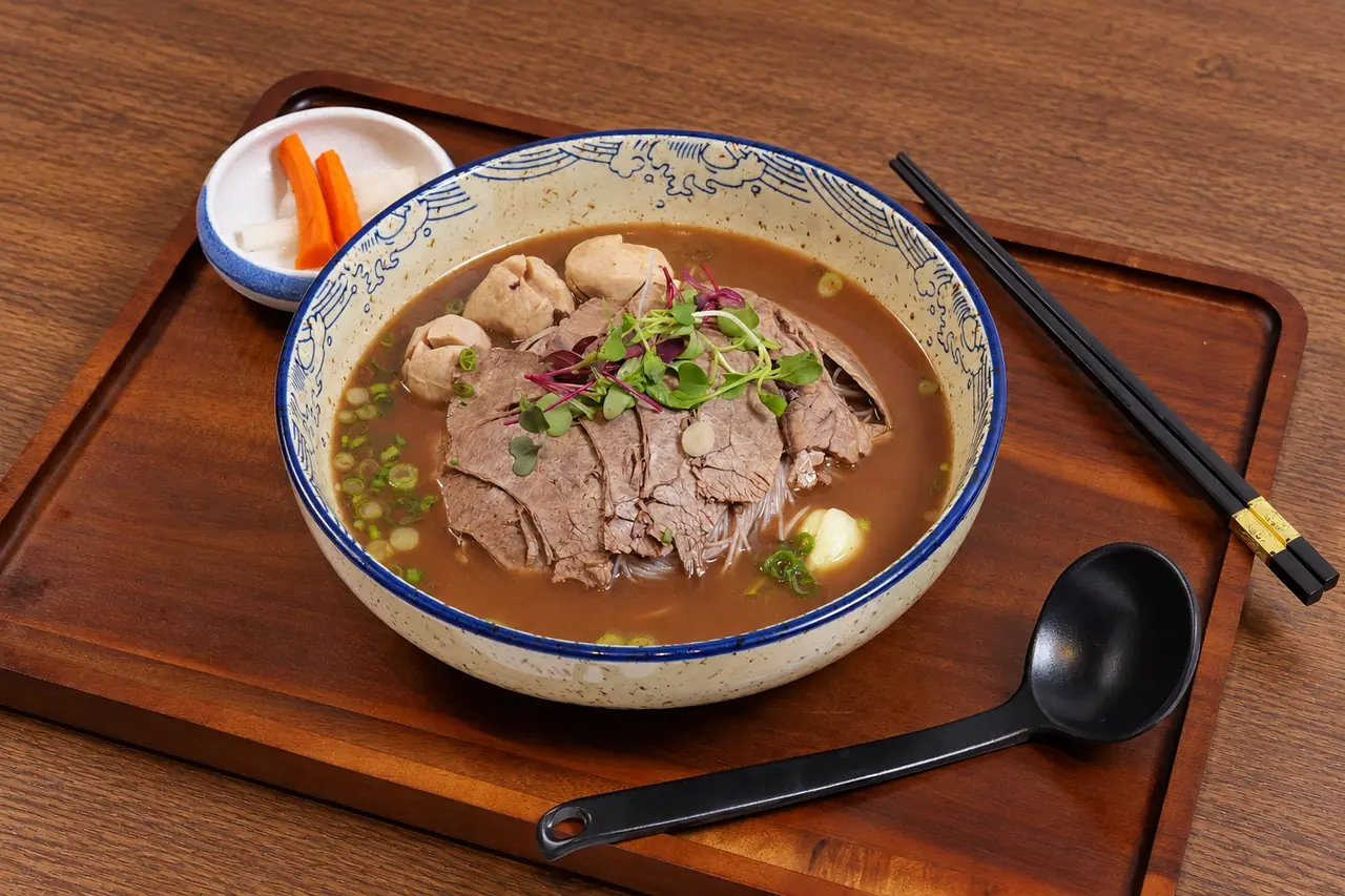 Midnight Boat Noodles with sliced beef, meatballs and greens in a brown broth.