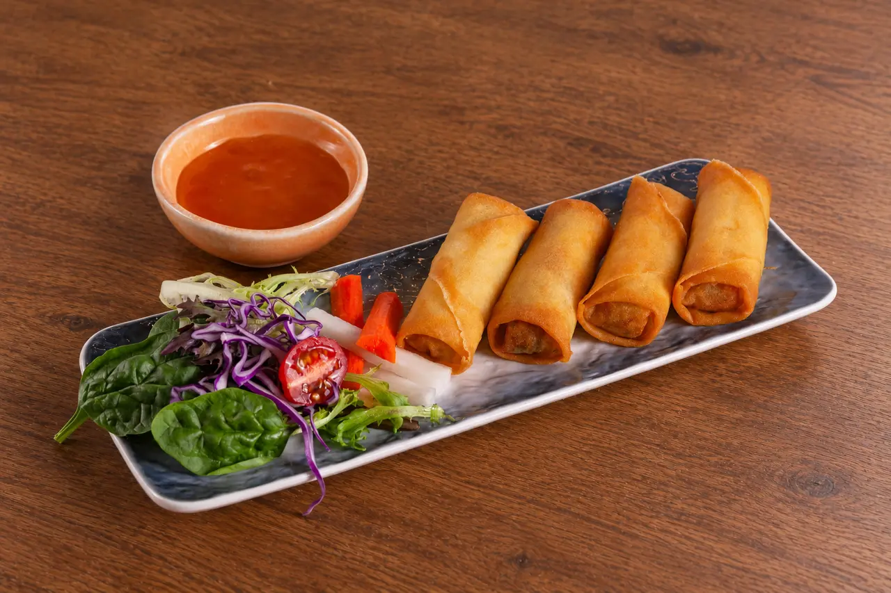 Four golden spring rolls with salad garnish and plum sauce.