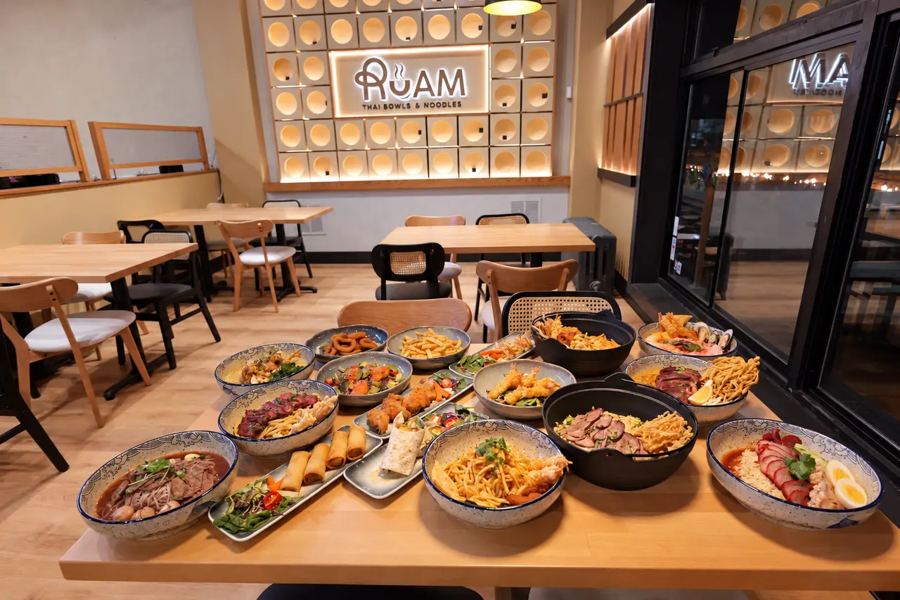A spread of RUAM noodle bowls and small plates on a restaurant table.